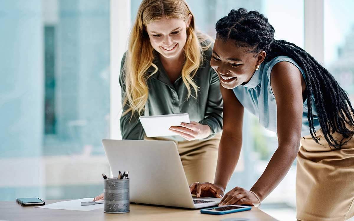 Zwei Frau blicken im Büro lachend auf einen Laptop