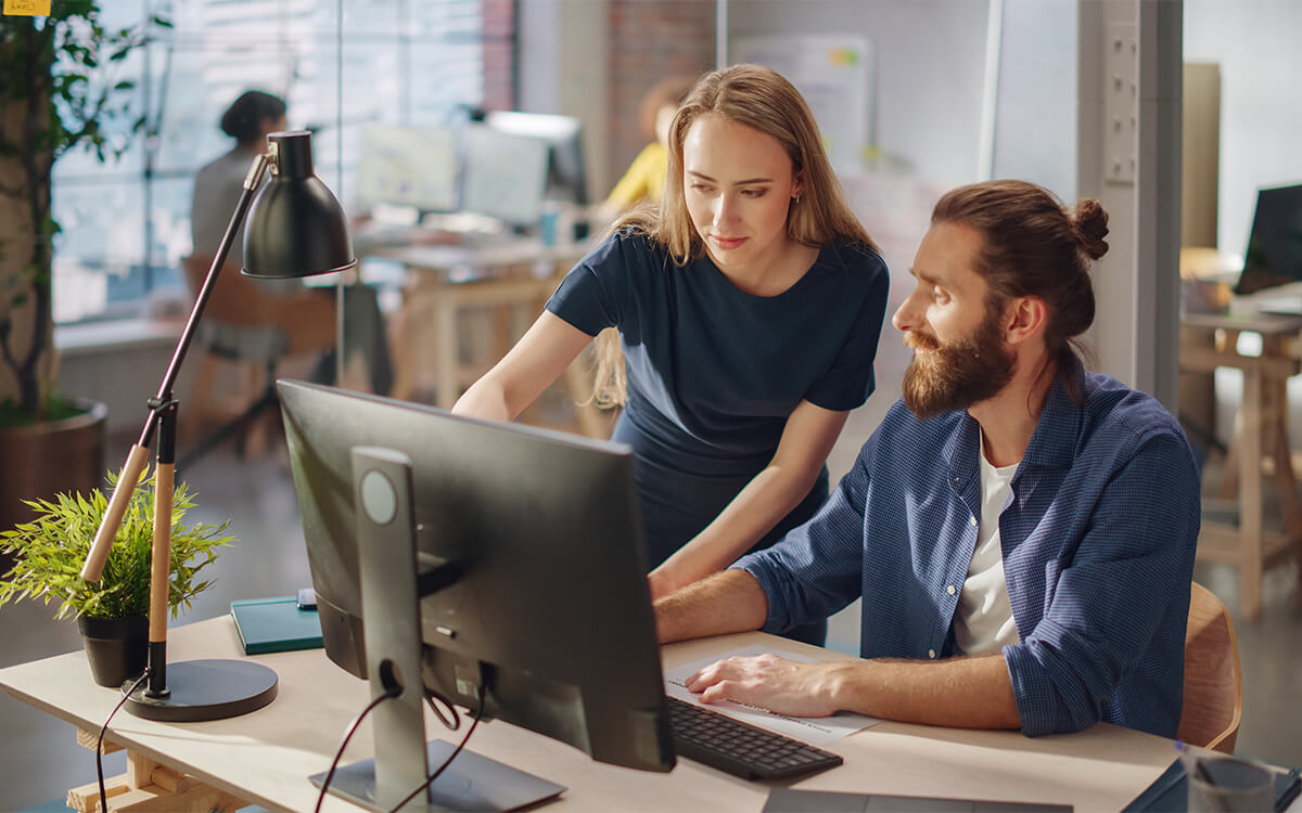 Eine Frau und ein Mann schauen auf einen PC-Monitor