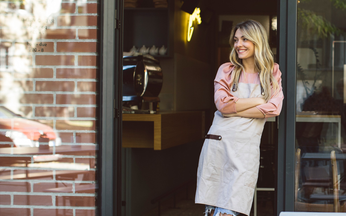 Eine Unternehmerin lehnt an der Eingangstür ihres Cafés