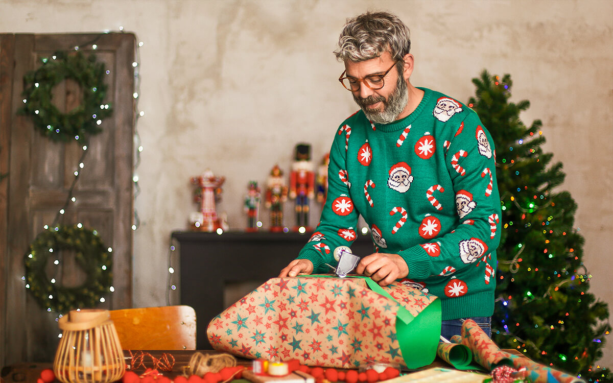 Ein weihnachtlich gekleideter Mann packt Geschenke aus
