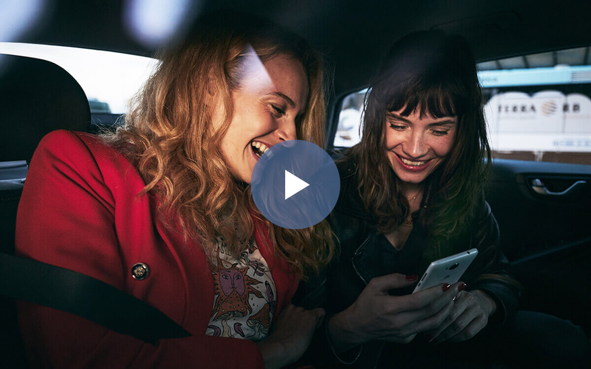 Zwei Frauen sitzen im Fond eines Autos und schauen lachend auf ein Smartphone