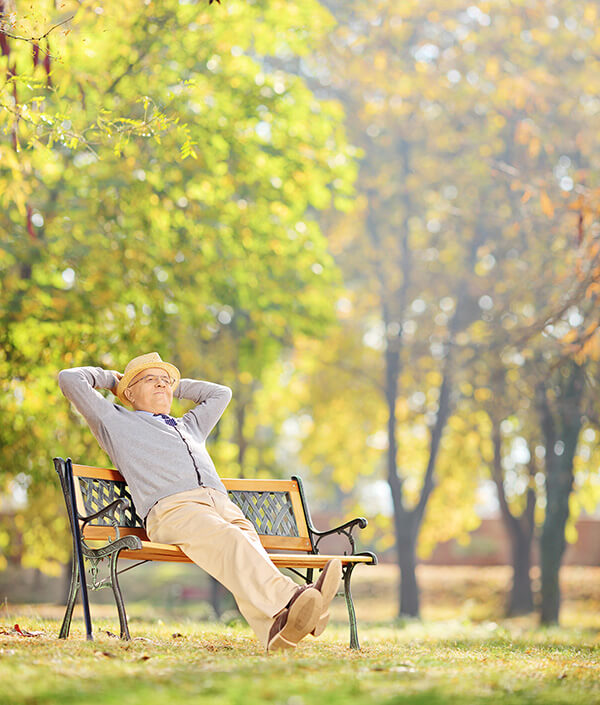 Mann sitzt entspannt auf einer Bank in einem sonnigen Park