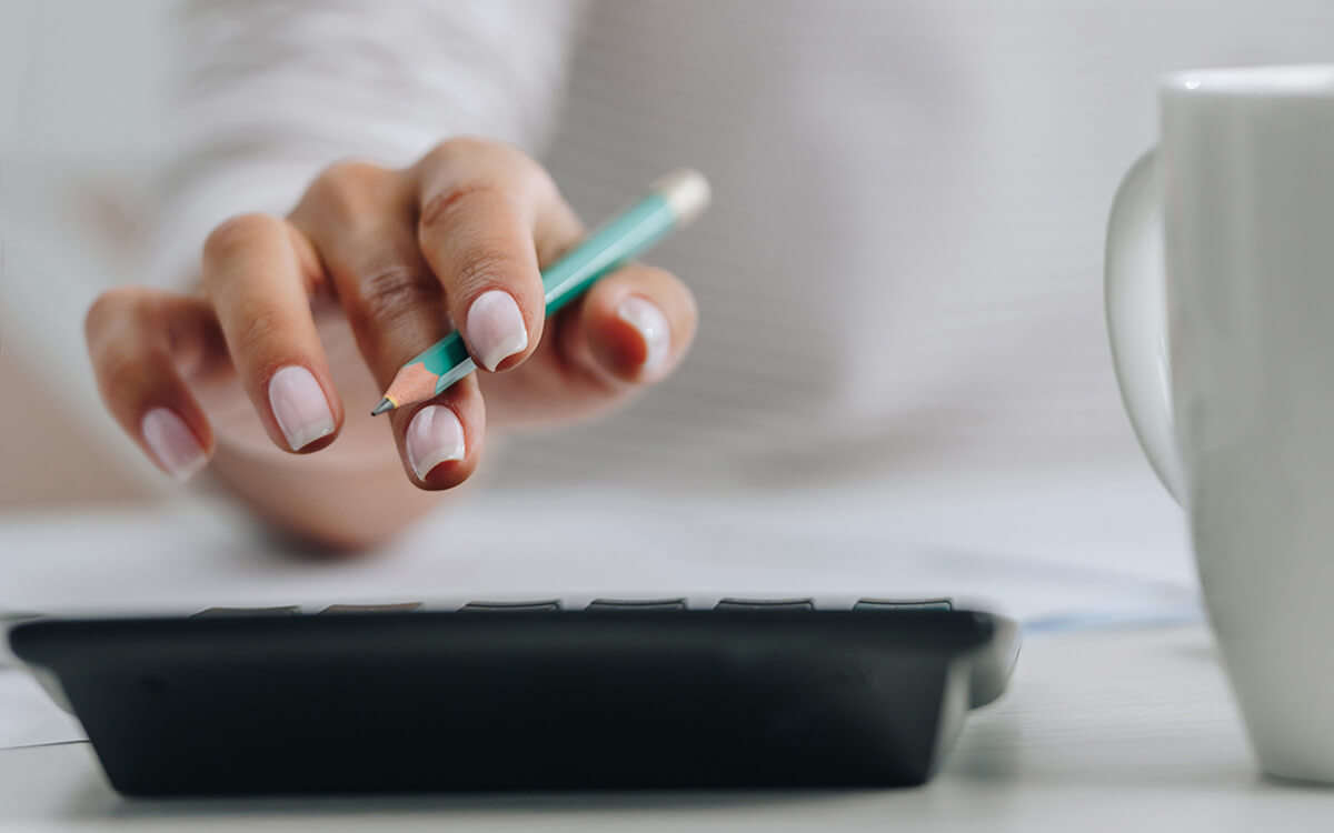 Frau mit Bleistift in der Hand bedient einen Taschenrechner