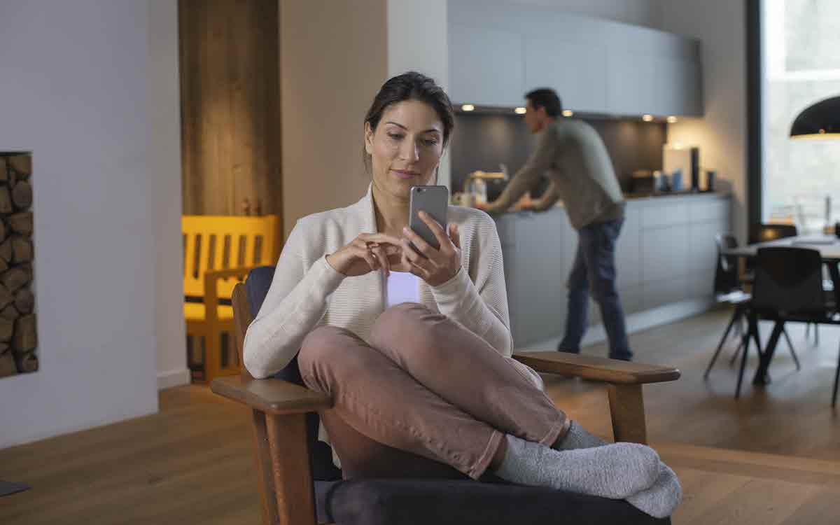 Junge Frau sitzt gemütlich auf einem Stuhl und schau in Ihr Handy