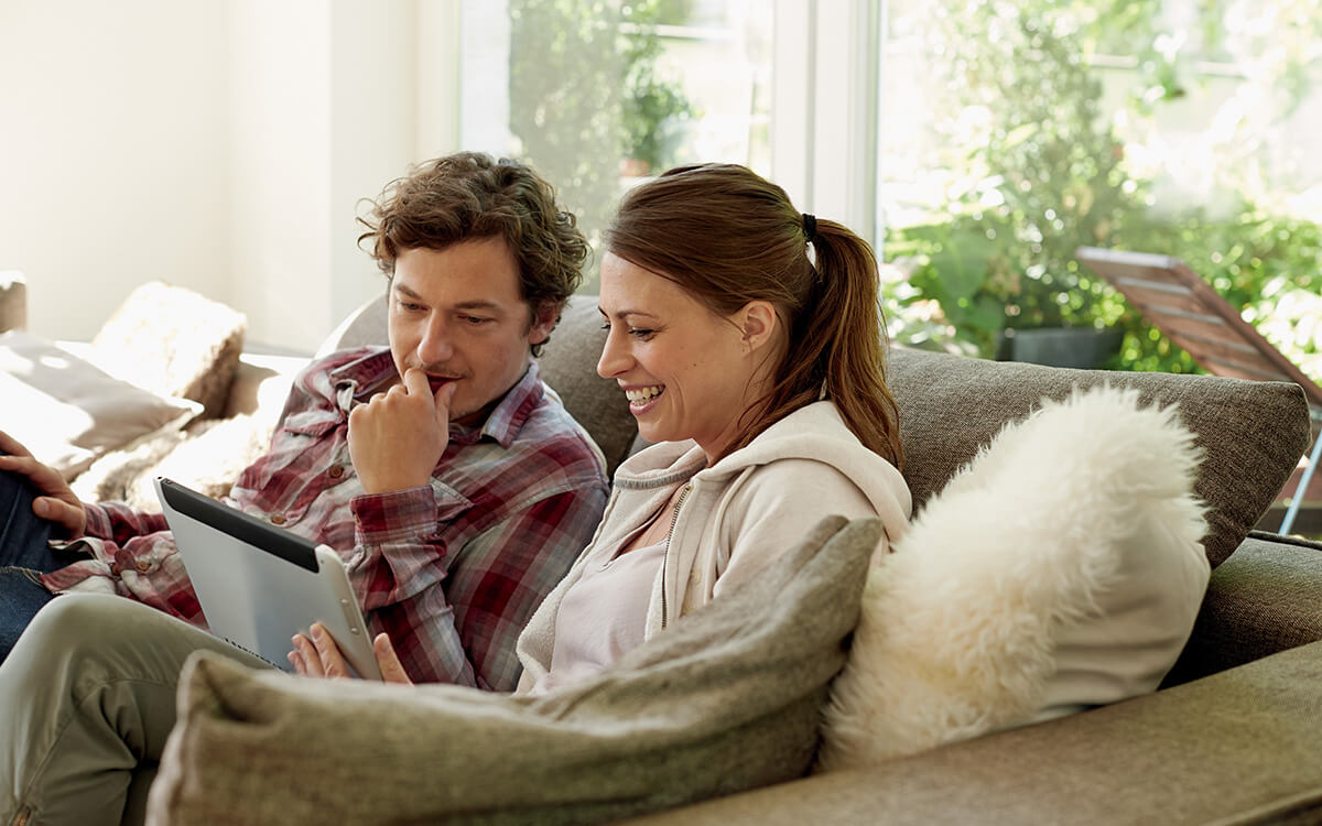 Ein Paar sitzt auf einer Couch und schaut gemeinsam auf ein Tablet