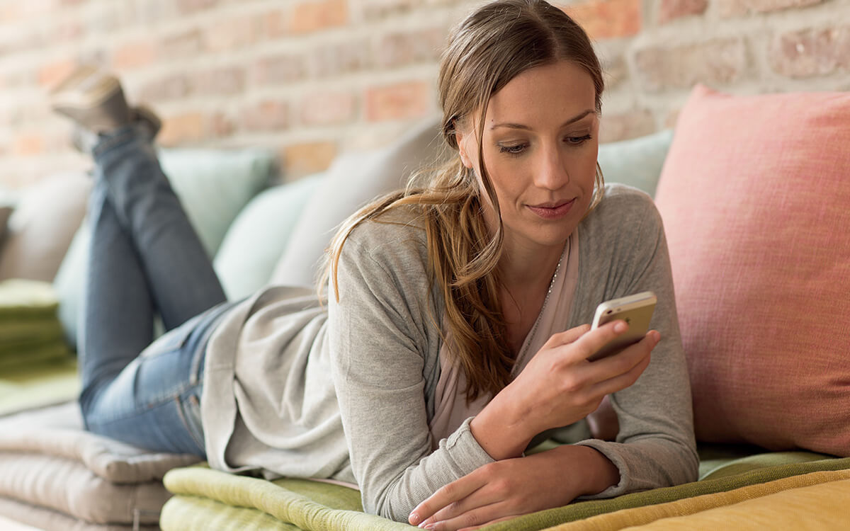 Eine Frau liegt auf der Couch und bedient ihr Mobiltelefon