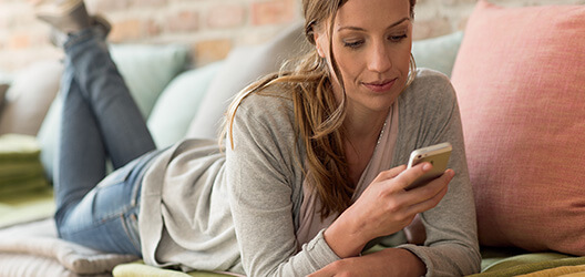 Eine Frau liegt auf dem Sofa und schaut auf ihr Mobiltelefon