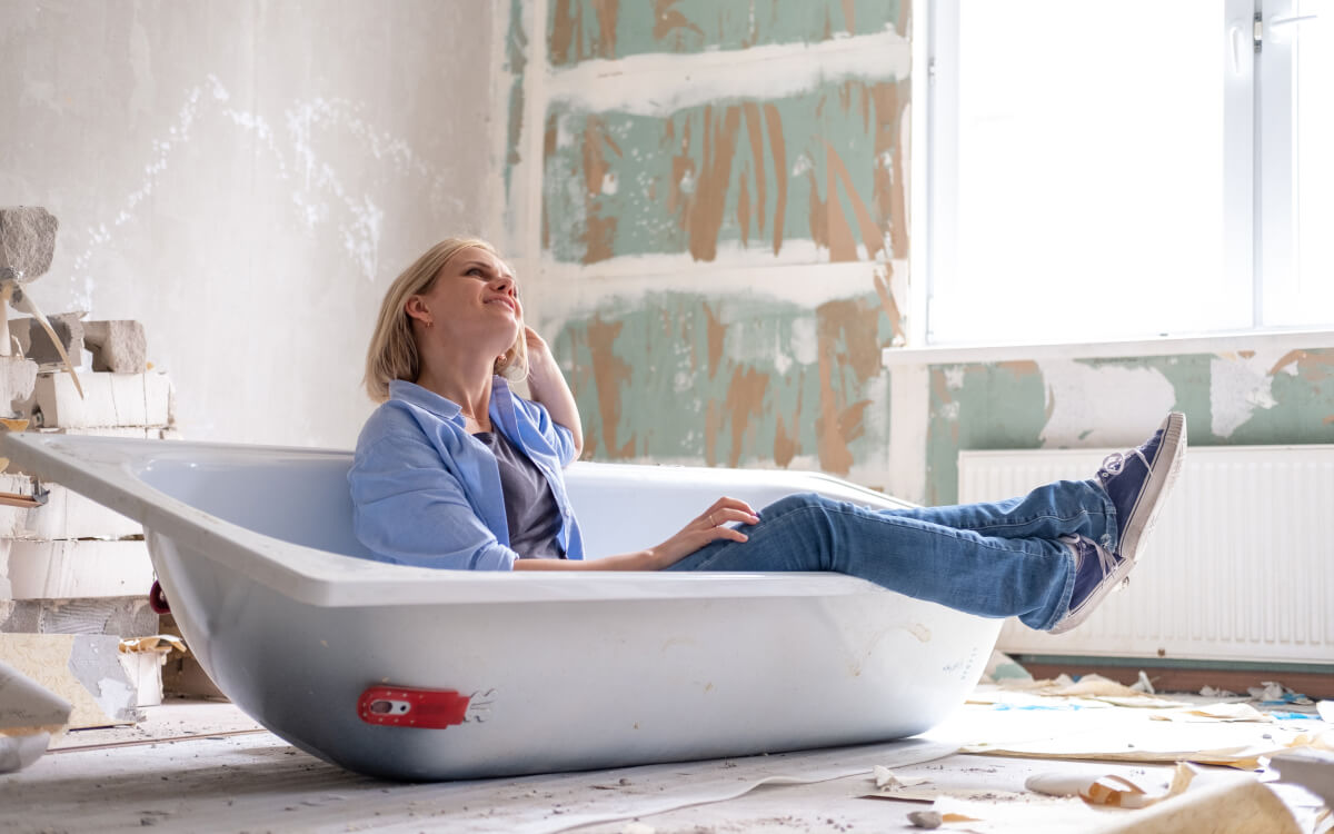Eine Frau sitzt in einer noch nicht eingebauten Badewanne, die sich in einem Zimmer im Rohbauzustand befindet