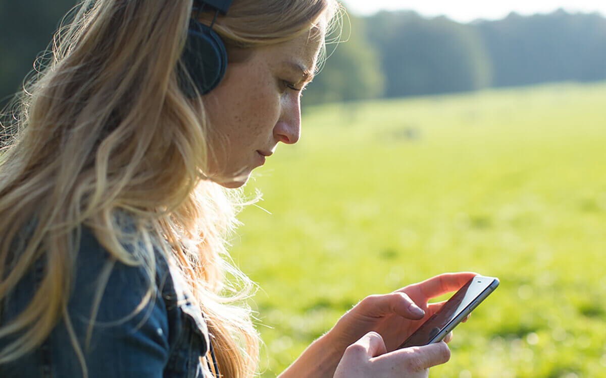 Eine Frau auf einer Wiese, die konzentriert auf ein Handy schaut